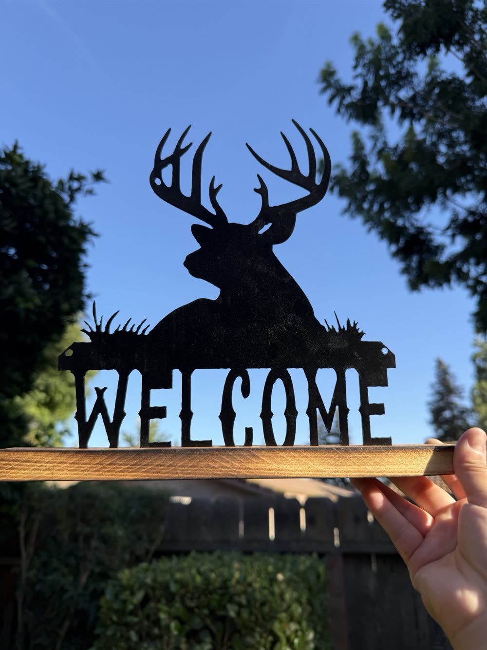 A steel WELCOME sign with a buck cut above the letters, on a wood base.