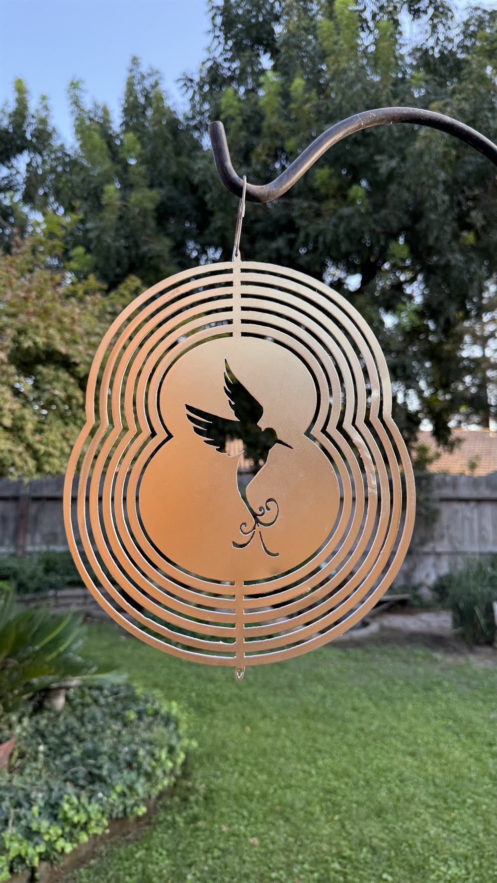 A steel hummingbird wind spinner hanging from a shepherd's hook.