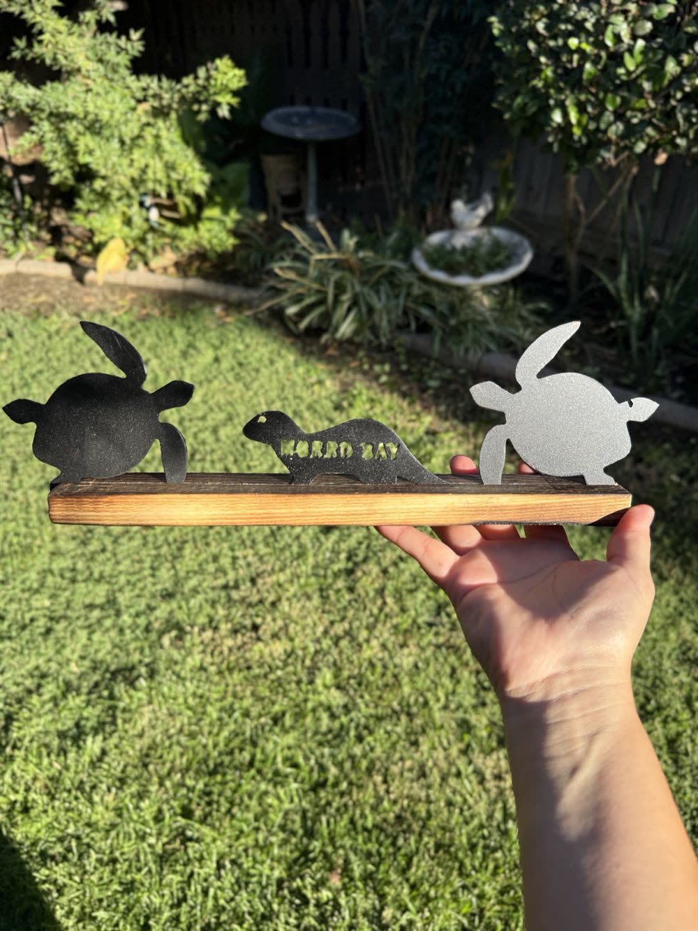 Two turtles and an otter cut from steel, on a wood base.
