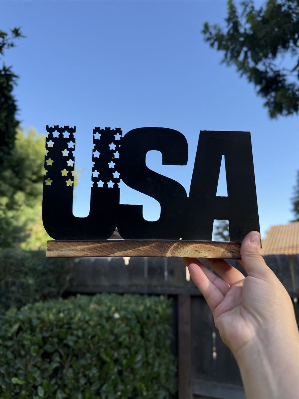 The letters USA cut from steel with a star-cut flag, on a wood base.